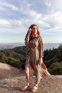 Full length of smiling young woman standing on land against sky