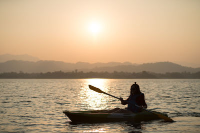 Man sitting in boat on lake against sky during sunset