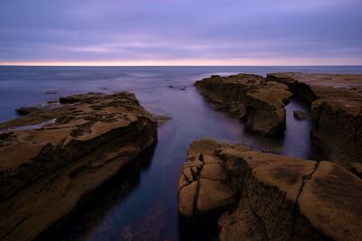 Rocks on beach against sky during sunset