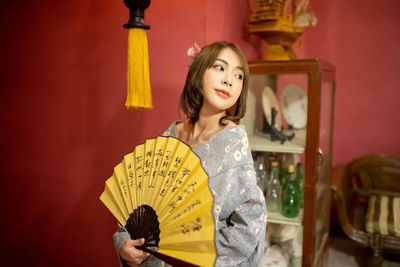 Close-up of woman holding hand fan at home