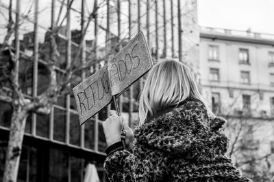 Rear view of woman holding umbrella against city