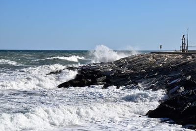 Sea waves splashing on rocks against clear sky