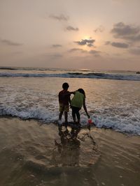 Rear view of siblings on beach against sky during sunset