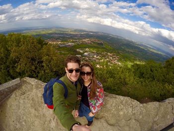 Portrait of smiling young couple standing on mountain peak against landscape