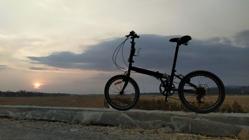 Bicycle on street against sky during sunset