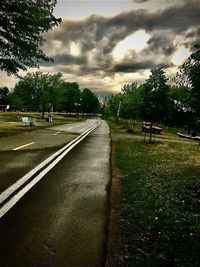 Road amidst field and trees against sky