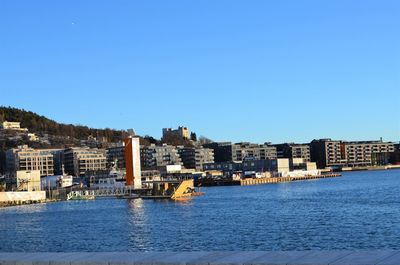 Buildings by river against clear blue sky