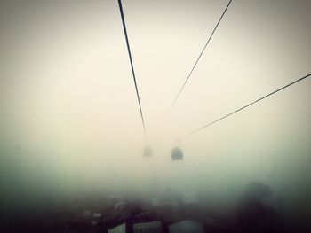 Low angle view of overhead cable car against sky during foggy weather