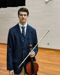 Portrait of young man holding violin while standing on hardwood floor