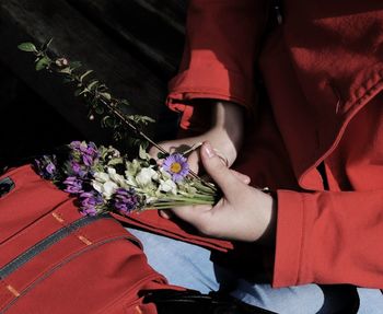 Midsection of woman holding flowers while sitting on bench