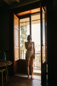 Rear view of woman standing against window at home