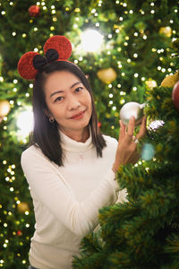 Portrait of young woman standing against christmas tree