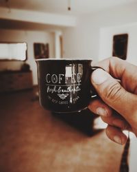 Cropped hand of person holding coffee cup with text at home