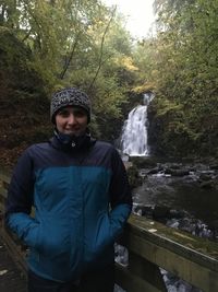 Portrait of man standing against waterfall in forest