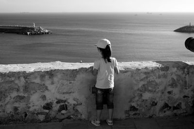 Rear view of girl standing by retaining wall against sea