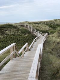 Empty wooden walkway leading towards landscape against sky