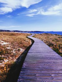 Boardwalk leading towards landscape against blue sky