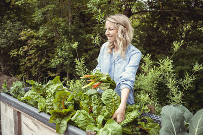 Full length of smiling woman standing by plants