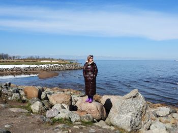 Rear view of woman standing on rock by sea against sky