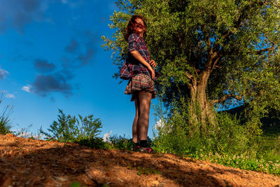 Woman standing by tree against blue sky