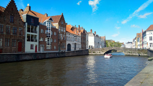 Bridge over canal by buildings against sky in city