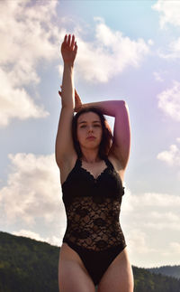 Beautiful young woman with arms raised standing against sky