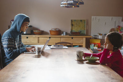 A father working on computer and child eating breakfast sit together