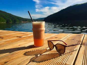 Drinking glass on table by lake against sky