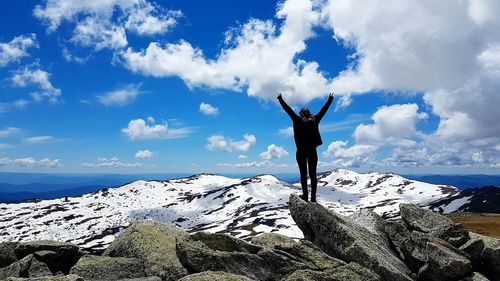 Rear view of woman standing on cliff against snowcapped mountains