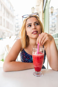 Portrait of young woman with drink sitting on table