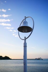 Street light by sea against sky during sunset