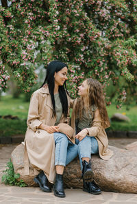 Mother and daughter relax in a spring blooming park, sitting on a stone