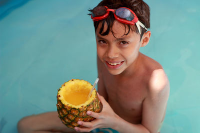 High angle portrait of boy having pineapple juice while sitting in swimming pool