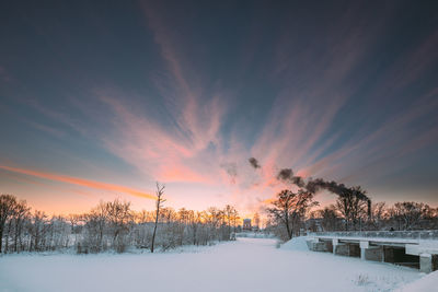 Snow covered field against sky during sunset