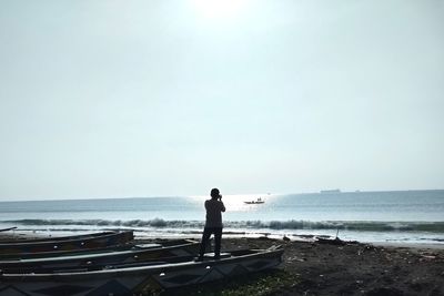 Rear view of man standing at beach against clear sky