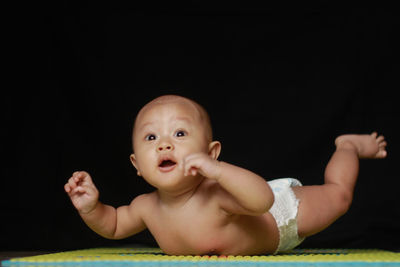 Portrait of cute baby girl lying on black background