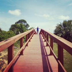 Footbridge by trees against sky