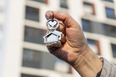 Keychain in house shape and key in male hand on background of new buildings