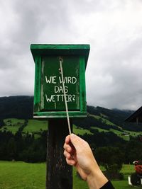 Close-up of hand holding information sign against sky