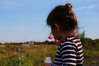 Close-up of girl blowing bubbles on field against sky