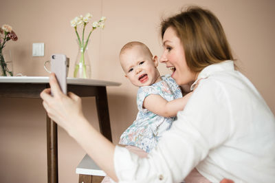 Mother does selfie with disgruntled little daughter in kitchen.