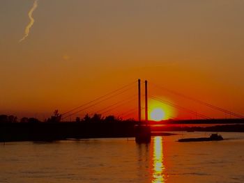 Silhouette bridge over calm sea at sunset