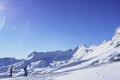 Man and woman walking on snowcapped mountains against blue sky during sunny day