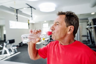 Senior man in fitness gym drinking water from bottle