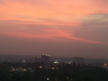 Illuminated city against sky at sunset