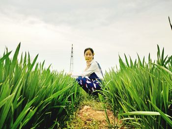 Portrait of smiling young woman standing on field against sky