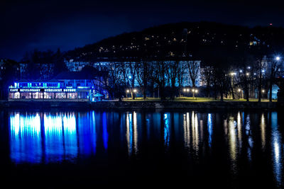 Illuminated city by river against sky at night