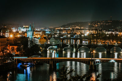 Illuminated bridge over river by buildings against sky at night