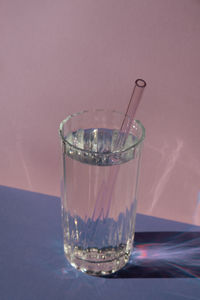 Reusable glass straws in glass with water on purple violet background eco-friendly drinking straw