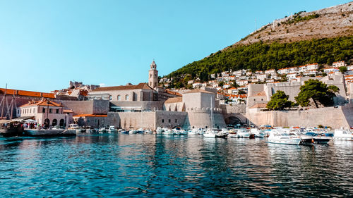 Sailboats moored on sea by buildings against clear sky